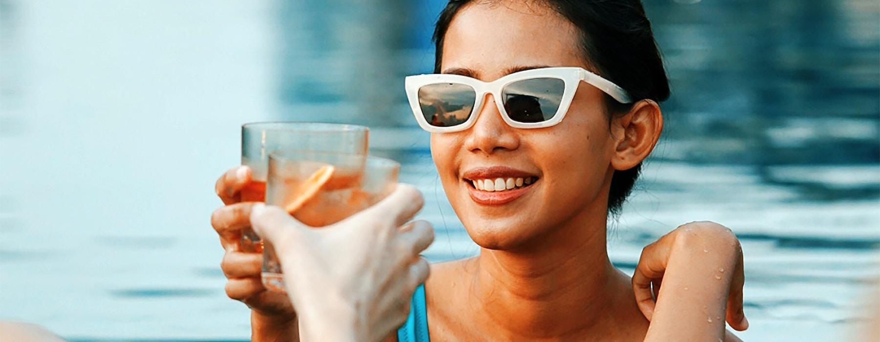 a woman in a pool holding a drink and a glass